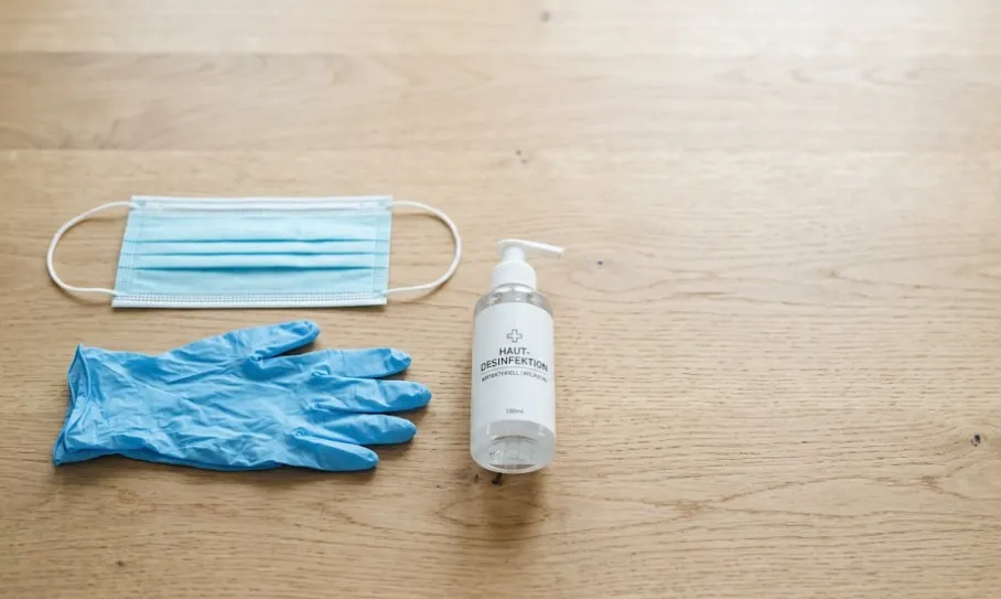Schutz-Set für Senioren: Einwegmaske, Handschuhe und Desinfektionsmittel auf einem Holztisch.